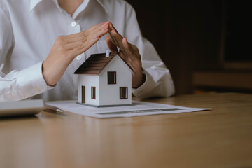 A businessperson presents a miniature house model on a contract document, symbolizing real estate investment, property sales, or home ownership.
