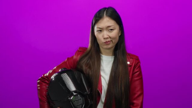 Woman in red jacket holding helmet against pink background, portraying a stylish and modern appearance with long hair and confident expression, showcasing individuality