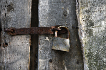 old padlock. Closeup view of an old padlock covered in rust, attached to a cracked wooden door. It represents themes of security, the passage of time, decay, and vintage aesthetics. the door is locked