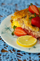 Piece of strawberry pie with lemon and fresh berries on lace light blue tablecloth