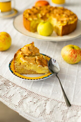 Homemade apple pie with custard cream on lace tablecloth, bouquet of red flowers and fresh apples