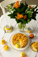 Homemade apple pie with custard cream on lace tablecloth, bouquet of red flowers and fresh apples