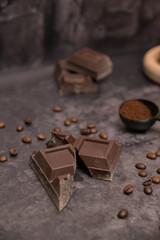 Close up. Pieces of broken dark chocolate on the table. Ground coffee in a black spoon. Spilled coffee beans. Dark background. Still life