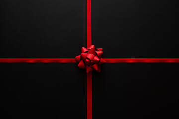 Black Friday background with a vivid red rosette bow centered on crossing red ribbons against a dark black background.