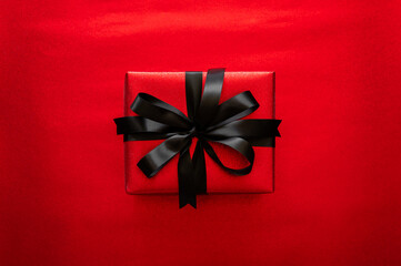 Black Friday concept with a striking red gift box with a black satin ribbon on a vibrant glitter red background for holiday sales.