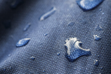 Macro close up of blue waterproof fabric with water droplet on hydrophobic textile surface. This resistant material shows quality protective properties
