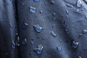 Close up detail of waterproof blue fabric with water droplet beading on wet surface. Repellent material texture shows feeling of protection from rain