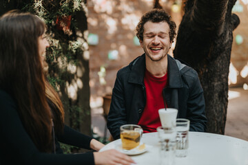 A cheerful young couple sitting at a cozy outdoor cafe, sharing laughter together with drinks on...
