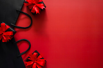 Black Friday concept with a black shopping bag and three gifts with red bows border a vibrant red background for sales text.