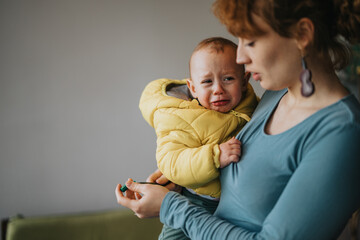 A caring mother calms a crying toddler, offering comfort and reassurance indoors. The intimate...
