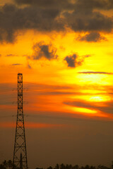 Naklejka premium The sunset silhouettes of the city's power line towers and communication antennas against a golden sky, reflecting industrial technology and construction.