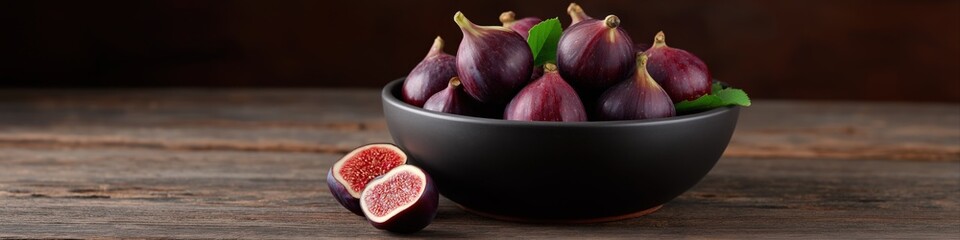 Fototapeta premium Fresh purple figs in black bowl on rustic wooden table with sliced fig