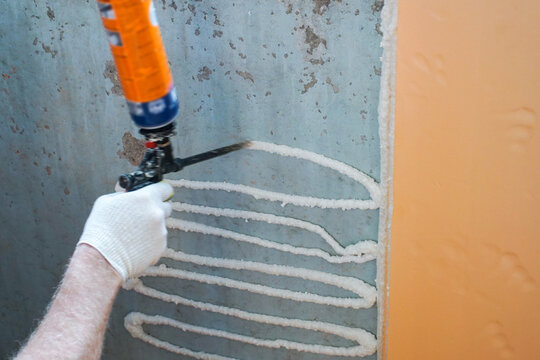 A worker applies adhesive foam sealant to a wall to bond insulation.