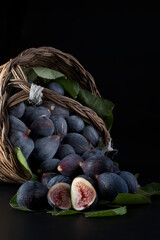 Fichi freschi in un cestino su sfondo nero con foglie.