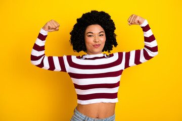 Confident woman flexing arms in striped top against vibrant yellow backdrop showcasing style and...