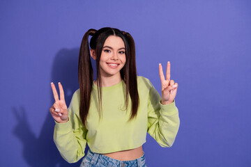 Smiling young woman with pigtails in a lime crop top showing peace gestures against a vibrant...