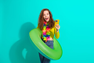 Cheerful young woman with curly hair using a smartphone while surrounded by vacation-themed...