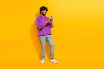 Young man with a stylish look uses smartphone, against vibrant yellow background, showcasing casual...
