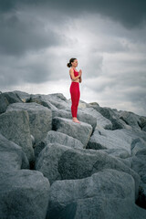 Woman wearing red sportswear standing meditating on rugged rocks, mountain pose