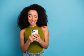 Charming young woman with curly hair using smartphone against bright blue background