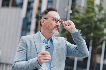 Professional city businessman adjusts glasses while holding smartphone in a stylish blue blazer...