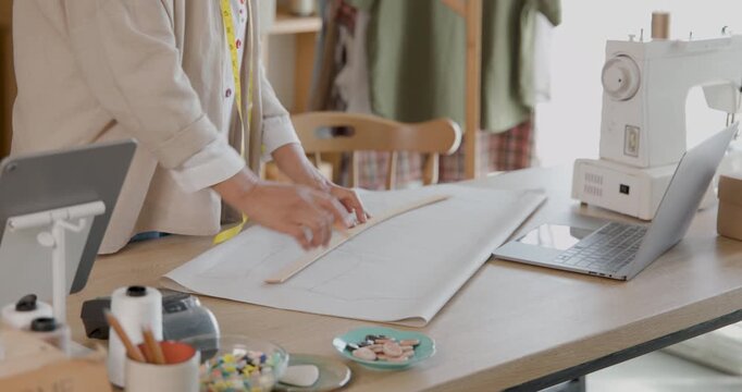 female tailor carefully drafting clothing pattern by hand on craft paper using sewing template at work table in sewing studio, 4k video.