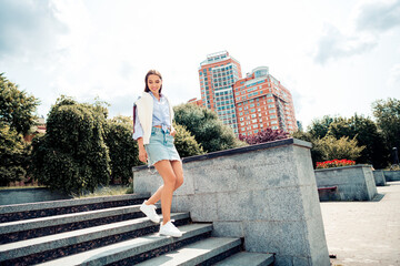 Lovely woman enjoying outdoor urban setting while walking stylishly dressed in casual spring outfit
