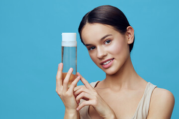 Young woman with a skincare bottle on a blue background showcasing healthy skincare, beauty, and...