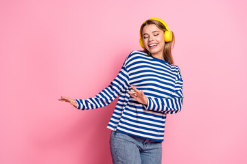 Smiling woman in casual fashion with yellow headphones enjoying music against a pink background