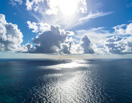 Aerial view of vast ocean under a sunlit sky with fluffy clouds - Powered by Adobe