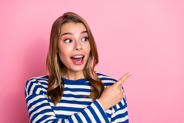 Joyful young woman in striped sweater pointing with enthusiasm against vibrant pink background