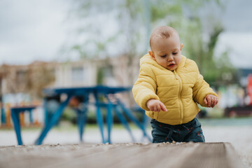Little child curiously observing surroundings in an outdoor setting, wearing a warm yellow jacket.