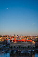 Evening sunlight bathes Prague Old Town, Czech Republic, with the Vltava River below and the moon rising in a clear sky- Vertical