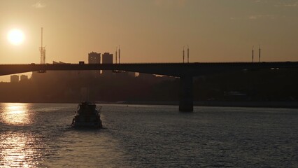 Passenger ferry crossing river at sunset under bridge. Clip