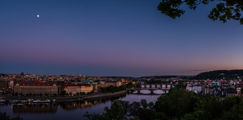 Panoramic twilight view of Prague Old Town, Czech Republic, with the moon shining above and street lights glowing, creating a peaceful and romantic atmosphere
