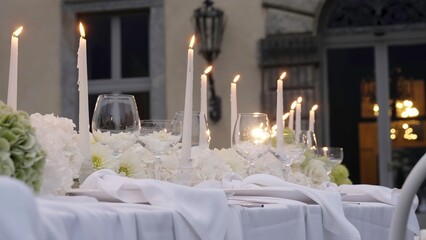 White candles burning on a wedding table set in front of a villa. Action