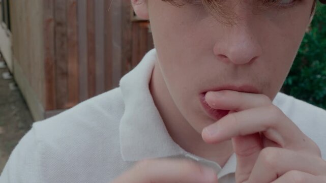 Close up of teenage boy pressing clear dental aligner firmly onto his upper teeth outdoors