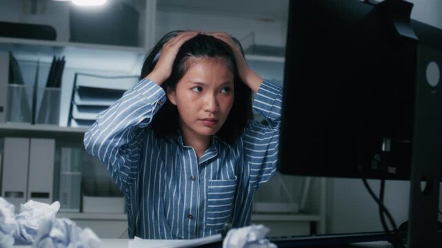 Tired and Stressed Young Asian Businesswoman Suffering from headache at desk in office. Asian female Office Employee sit at desk in office with mental health problem, making mistake, work deadline.
