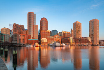 Naklejka premium The beautiful cityscape of Boston at dawn, showing the waterfront and buildings reflected in the calm water.