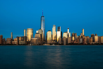 Fototapeta premium The illuminated New York City skyline of downtown Manhattan, with buildings glowing in the golden light of the evening.