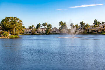 The serene residential area of Spring Lake in Naples, Florida, with large homes and tropical palm trees around a lake with a fountain.