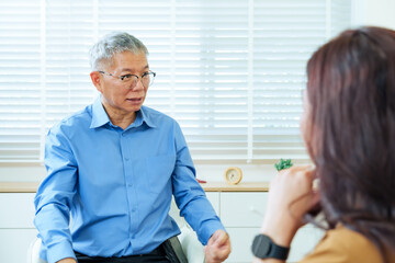 Obraz premium Senior male psychiatrist speaking gently to asian woman during therapy session offering emotional advice and professional guidance about relationship concern representing care trust
