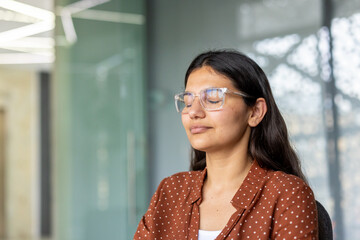 Young businesswoman meditating or relaxing with eyes closed and clear glasses, practicing...