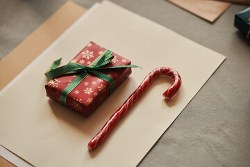 Christmas present wrapped in festive paper with green ribbon placed next to candy cane on table, celebrating holiday season with traditional gift and sweet treat arrangement