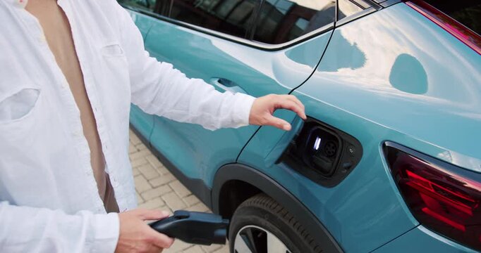 Close-up view of a man preparing an electric car for charging by opening the port and connecting the charger