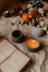Burning handmade candle in ceramic cup with open book and eucalyptus branch on rustic paper background