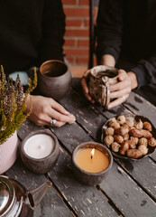 Cozy outdoor scene with burning handmade candles, hot tea and nuts on rustic wooden table