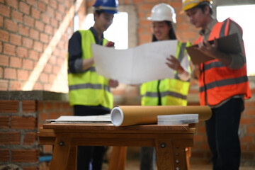 Selective focus on construction blueprints and tools on a wooden table, with engineer and technicians blurred in the background during a renovation project