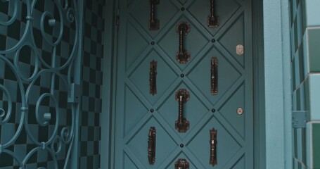Close up of an ornate teal door featuring geometric metalwork and intricate bronze handles.
