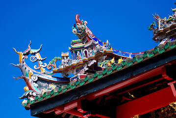 Fototapeta premium Intricate Chinese Temple Roof Ornament with Colorful Figures and Mythical Creatures Against Blue Sky